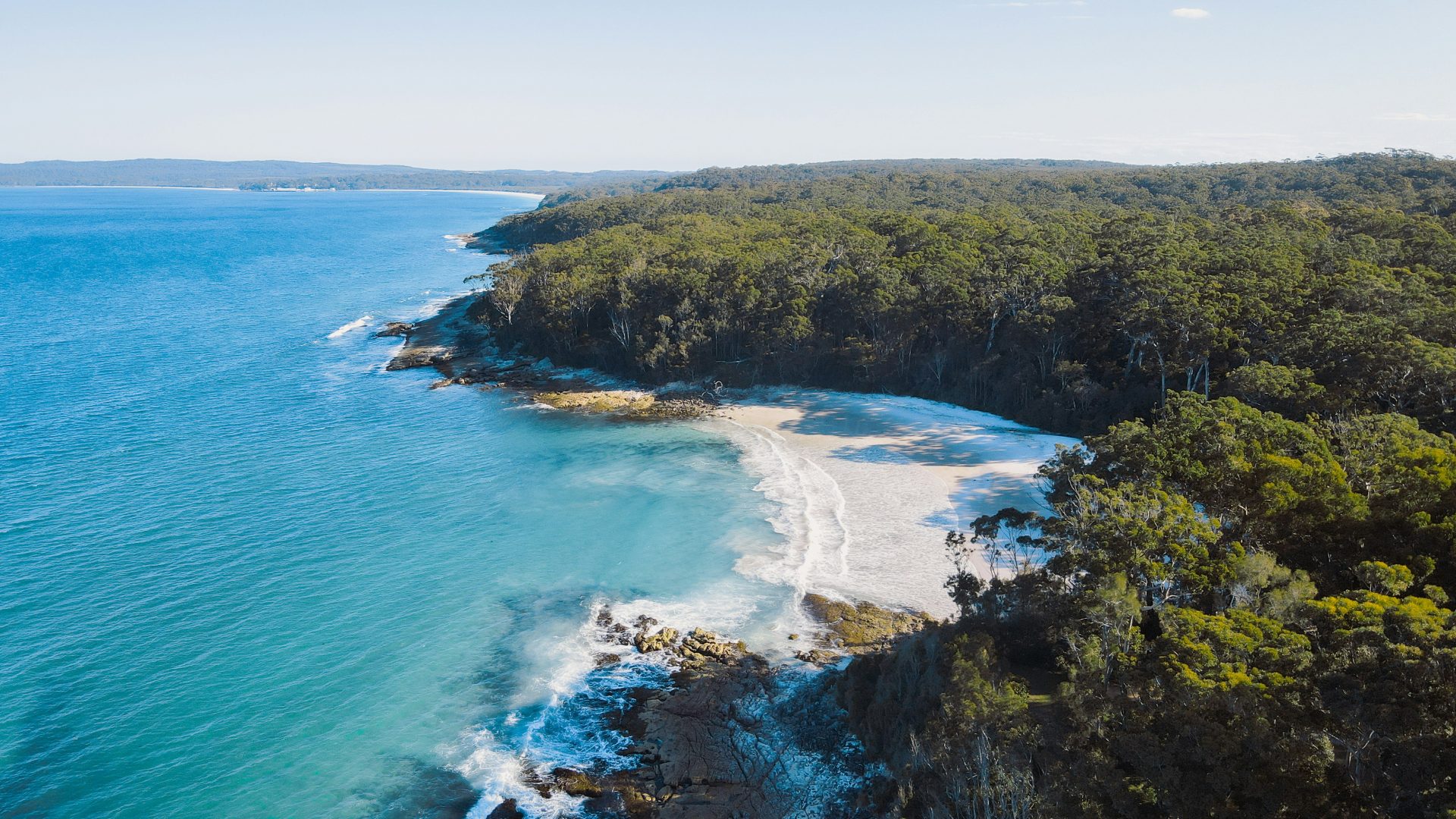 Aerial view over a cove and blue sea along a rugged coastline