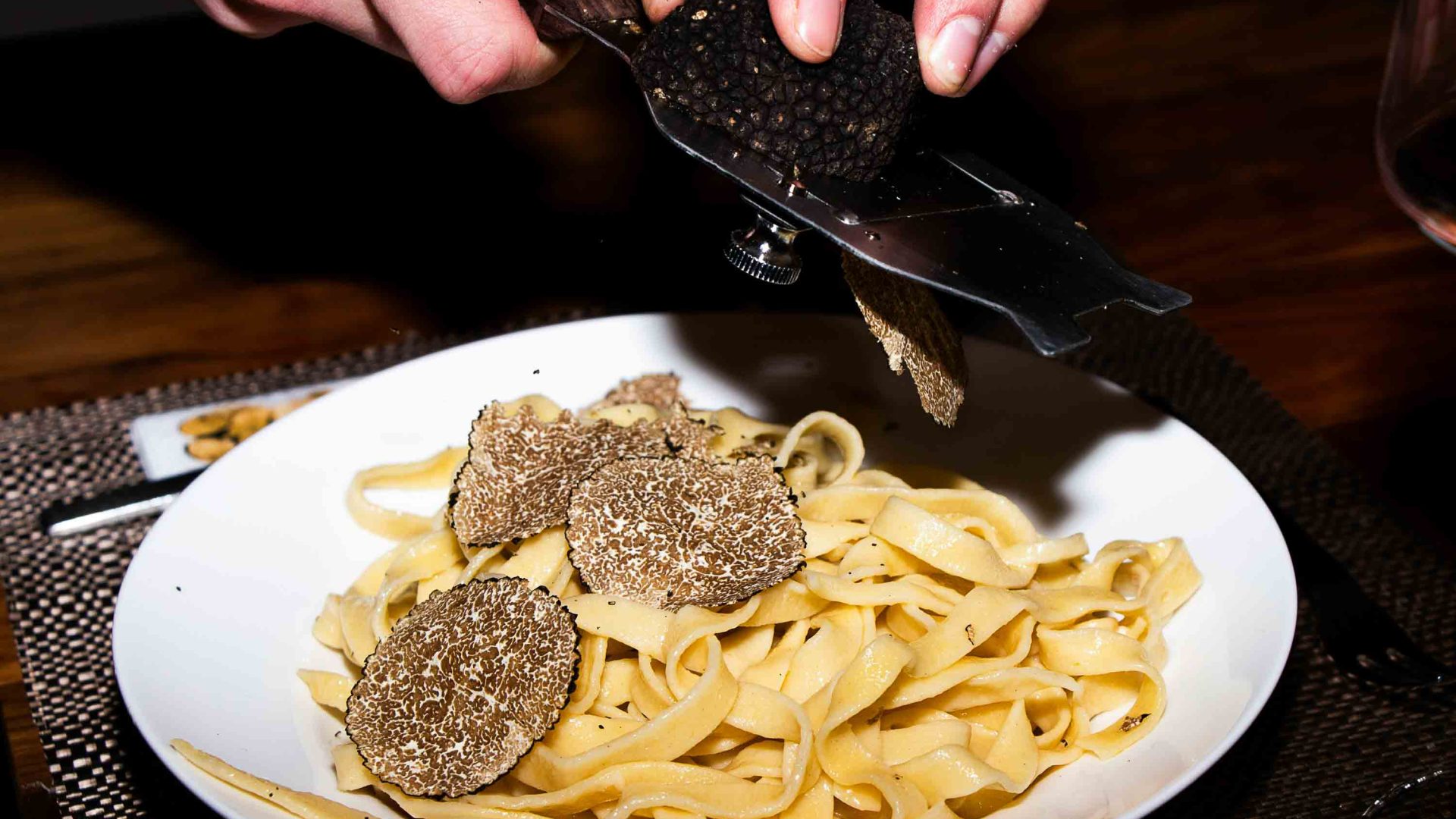 A hand grates truffles over pasta.