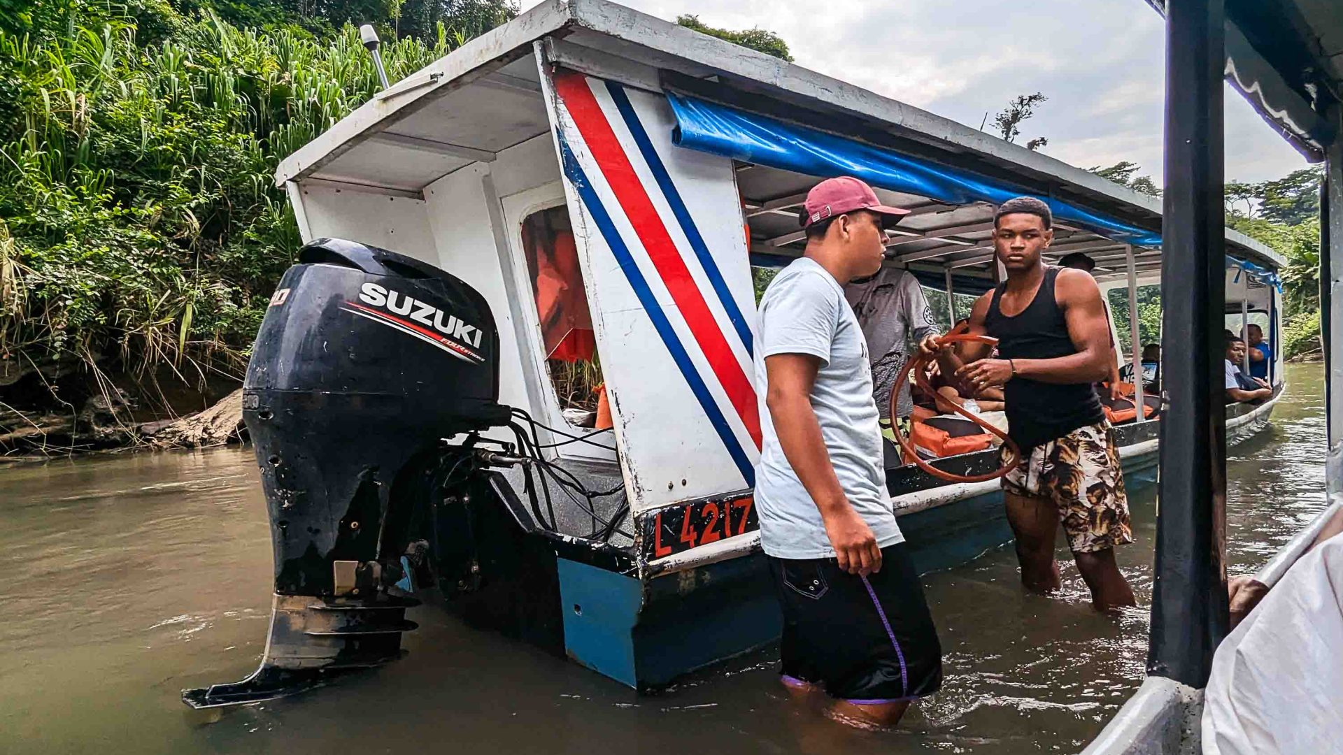 A couple of men siphon water from a boat.