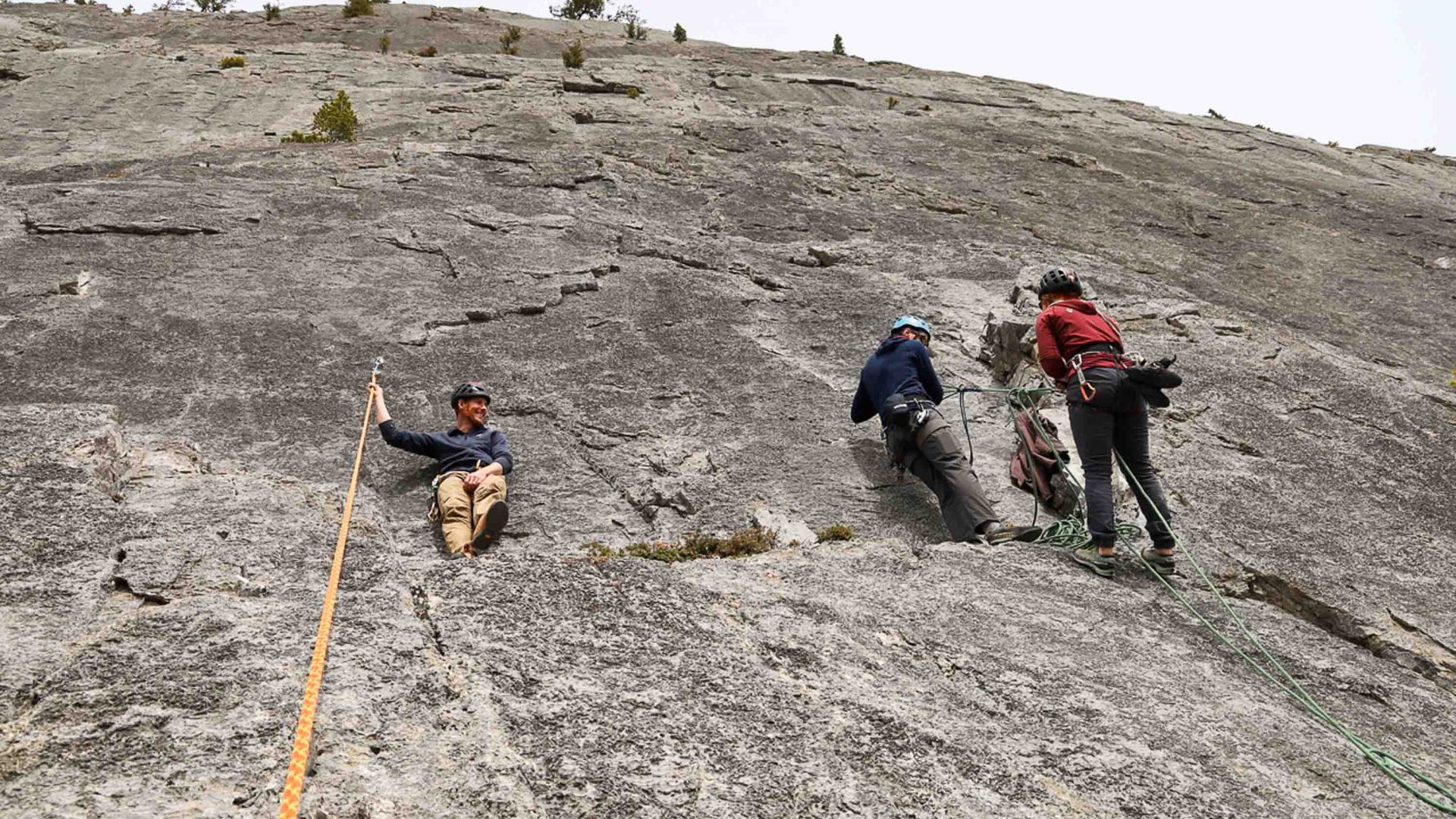 A male guide talks with others participating in mountaineering on the edge of a rock face.