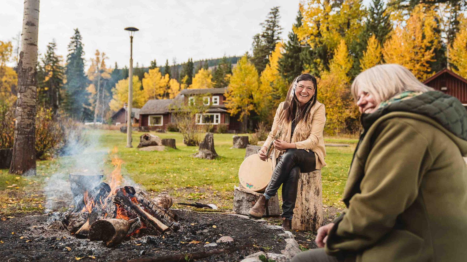 Matricia Bauer sits by a fire and laughs with another woman.