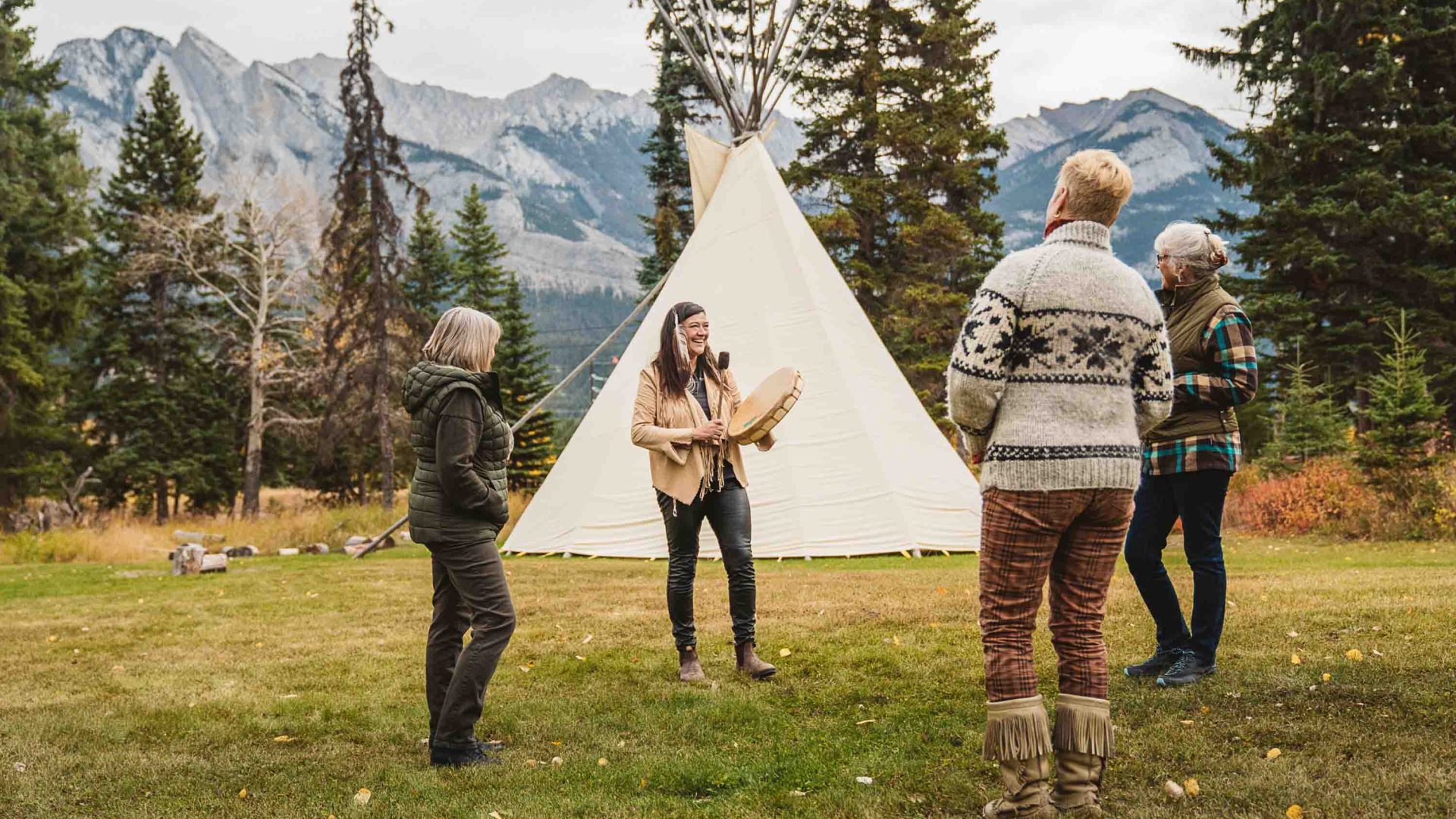 A woman stands in front of a tent and speaks to a group in front of her.