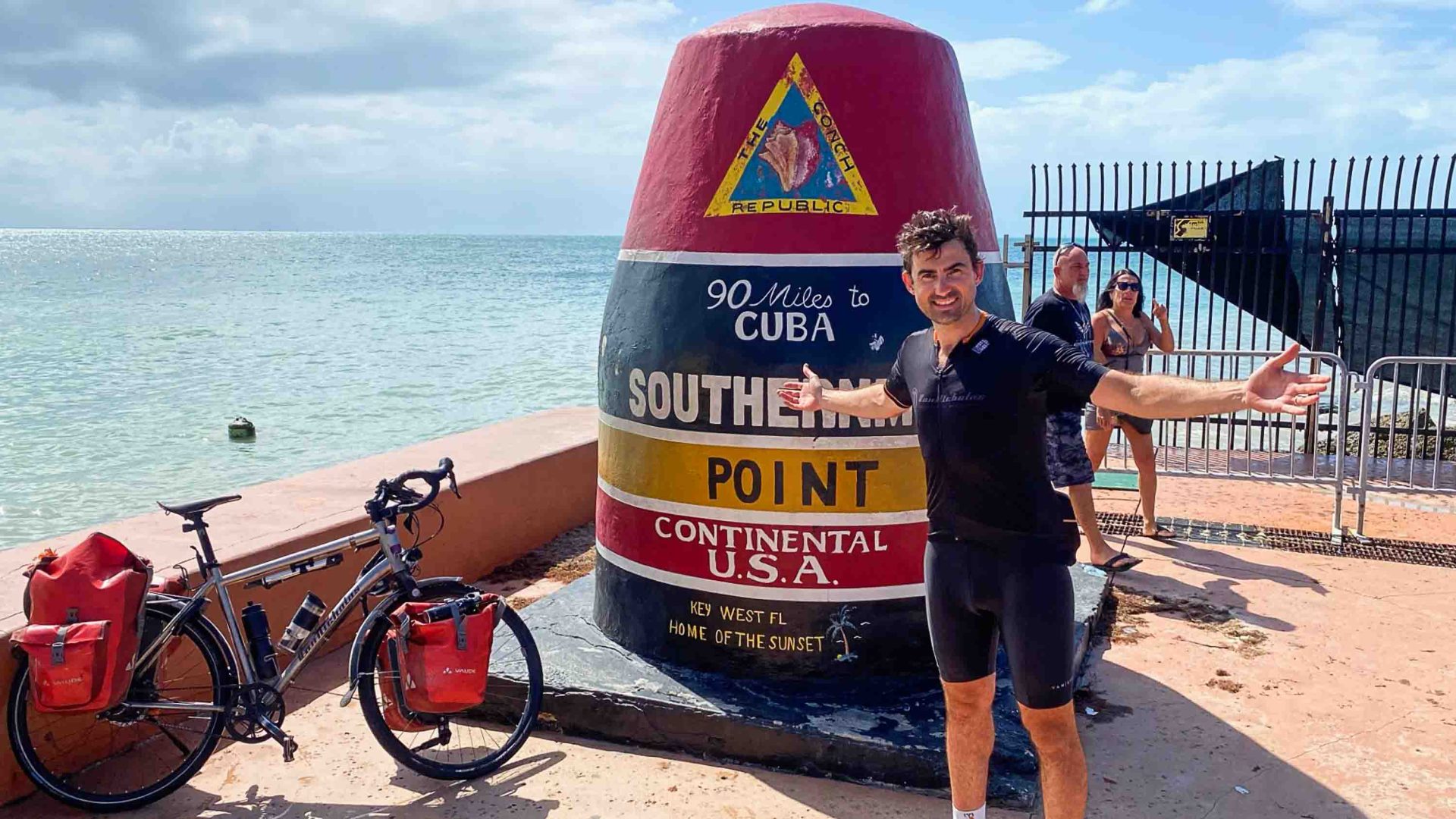 Simon has his arms outstretched at a sign for Key West.