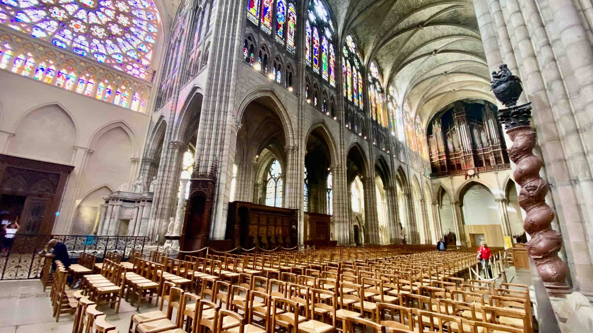 The interior of the Basilica of Saint Denis showing stained glass windows and pews.