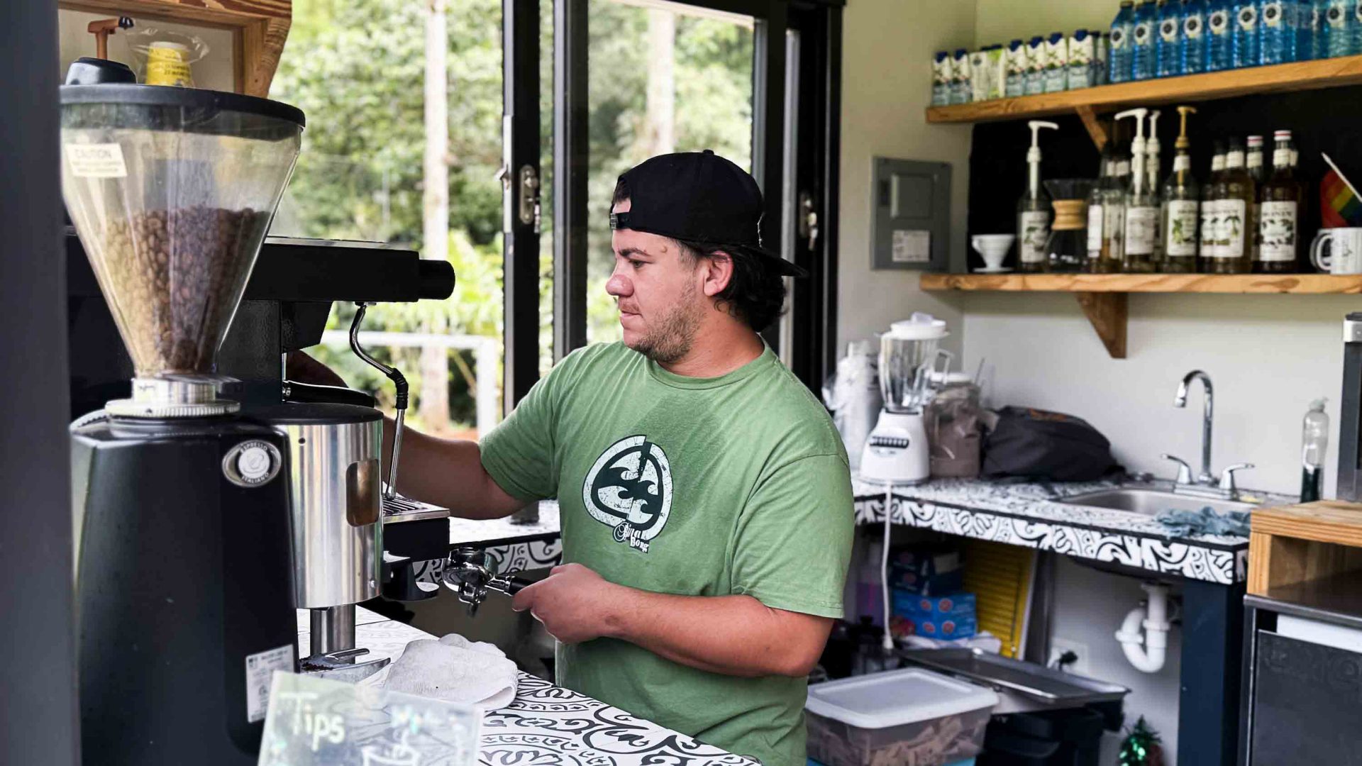 A man in a green t shirt makes coffee.