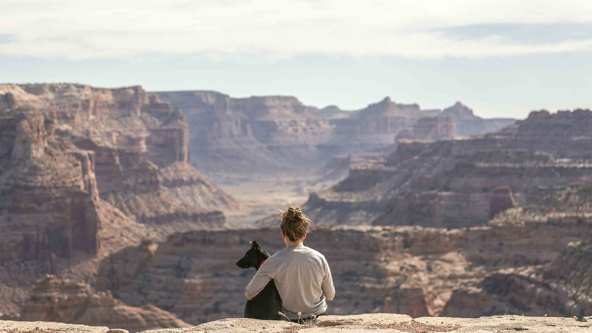 A woman sits and looks out over a canyon with her dog.