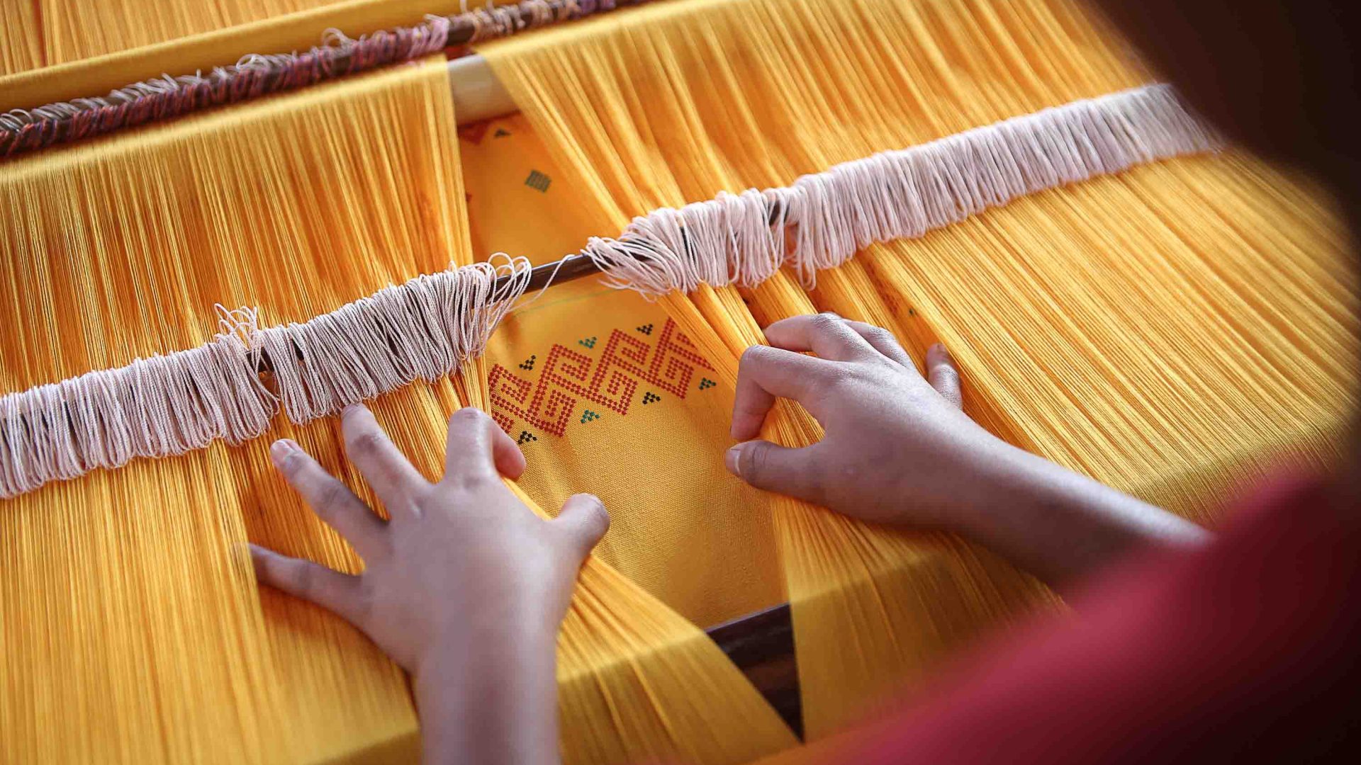 A woman weaves yellow fabric with red stiching in Indonesia.