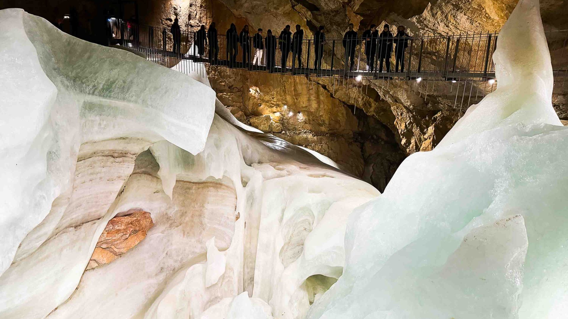 People stand on a walkway looking down at ice in a cave.