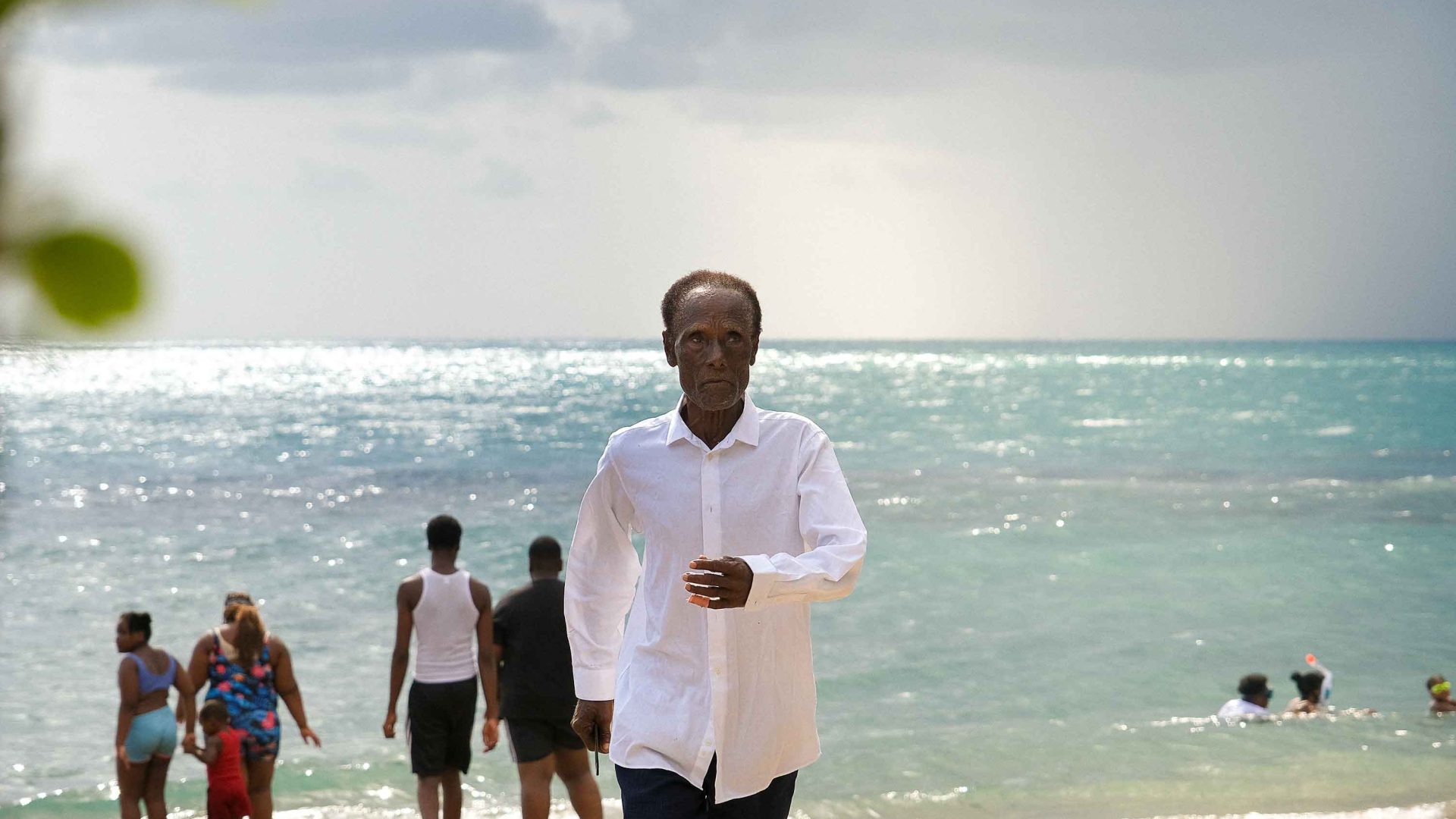 A man walks on the beach while others enjoy the waves.