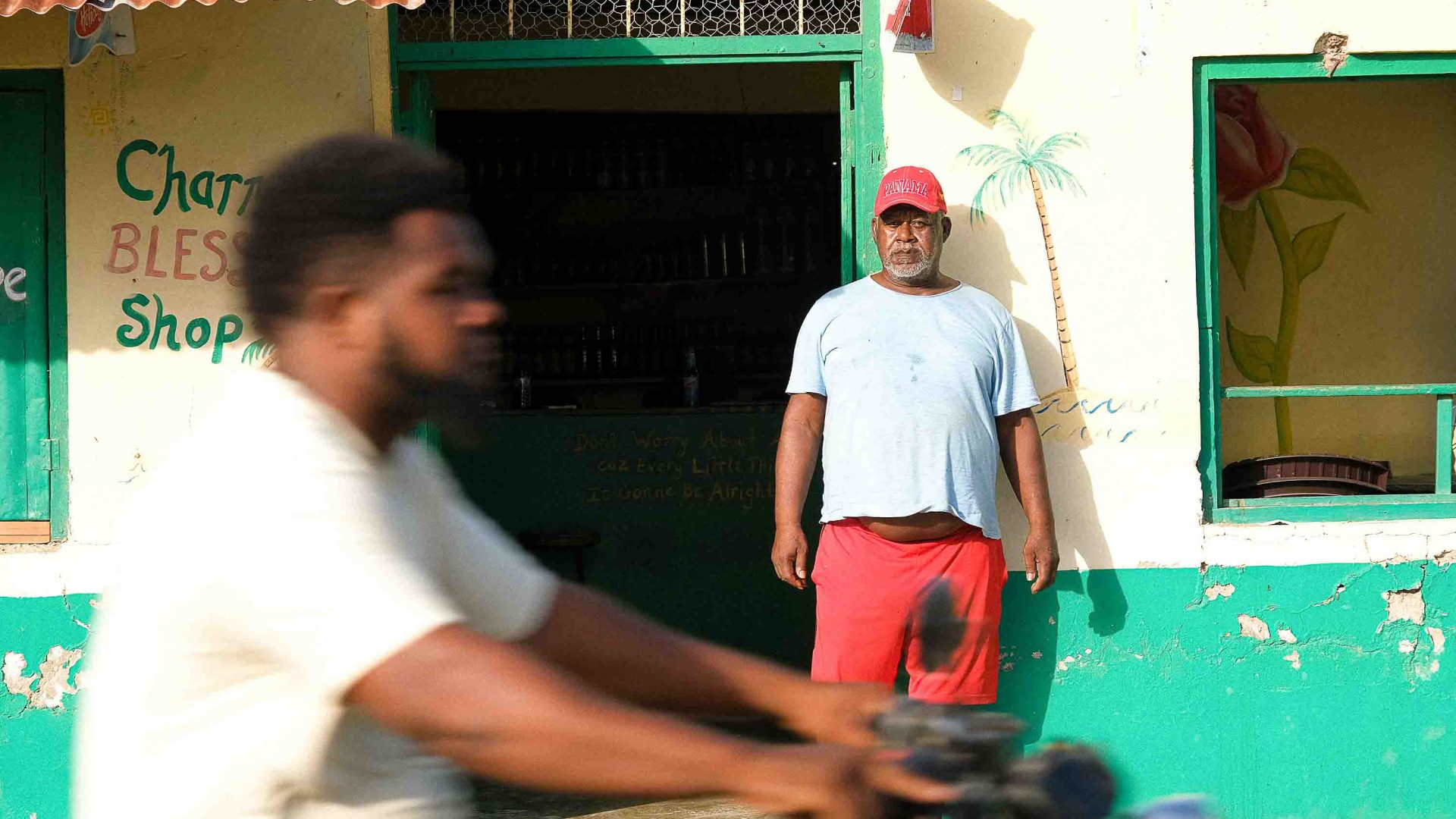 A man stands in front of his shop as a scooter goes past.