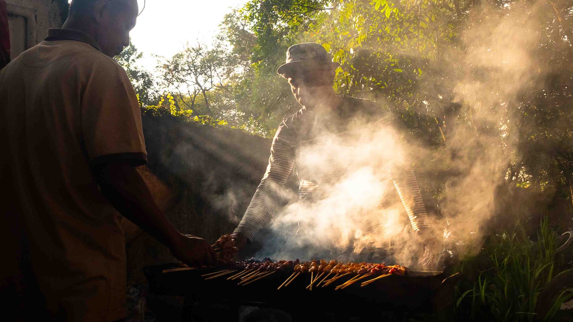 A man barbecues some meat. He is obscured by smoke.