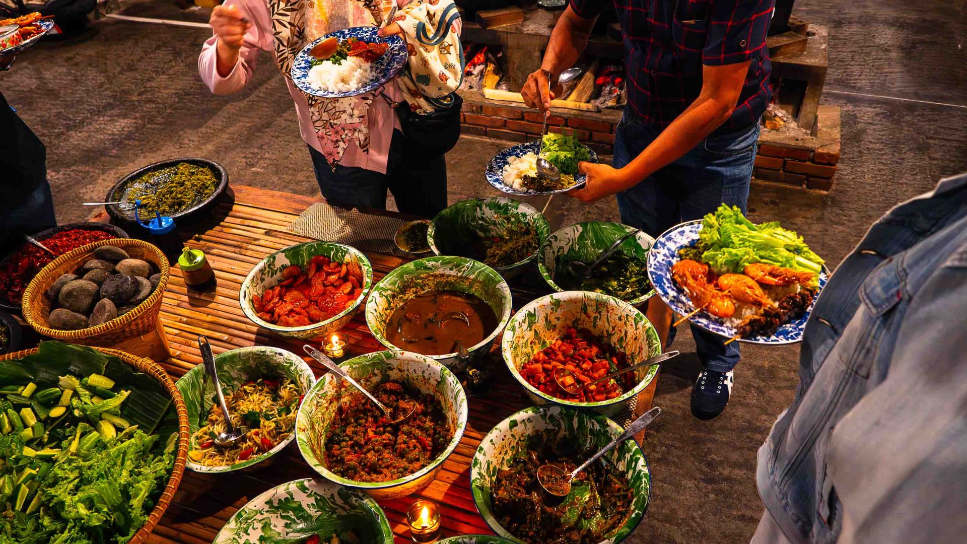 Hands reach pout above a table laden with colourful dishes.