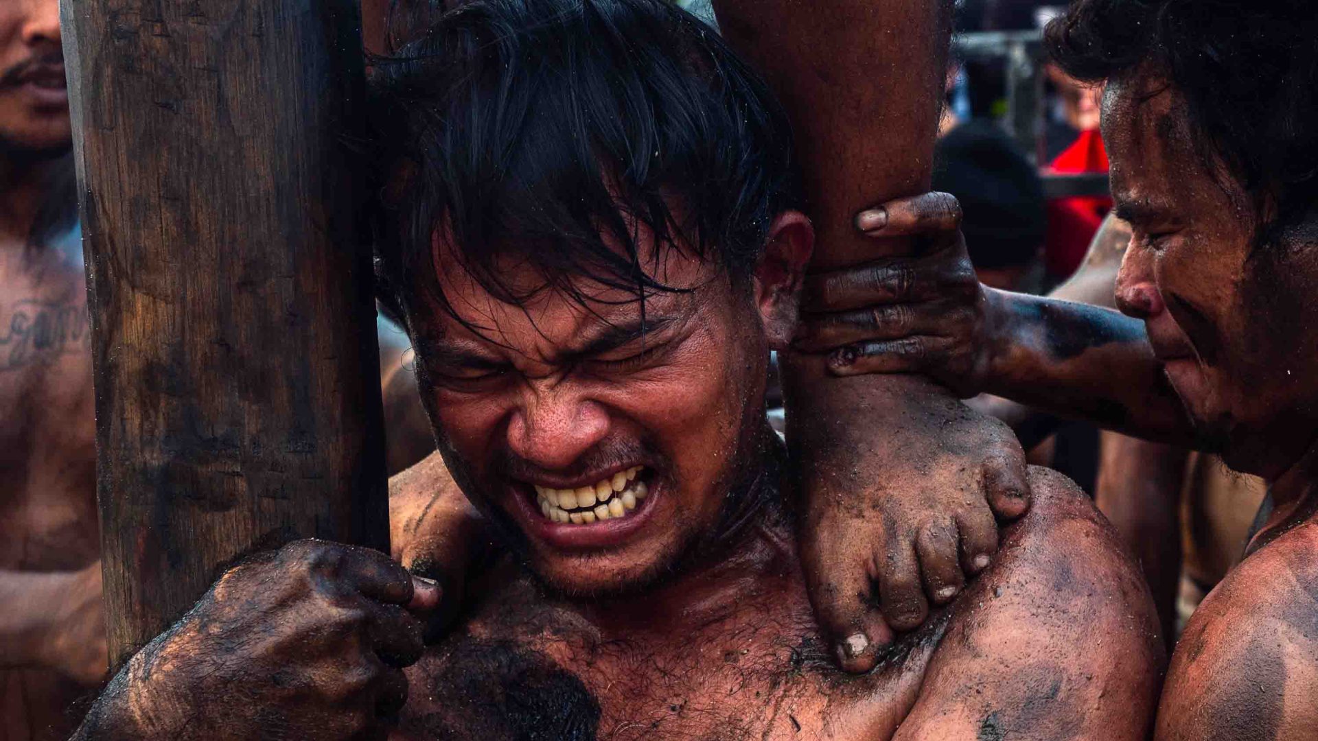 A man grits his teeth as another mans feet can be seen standing on his shoulders.