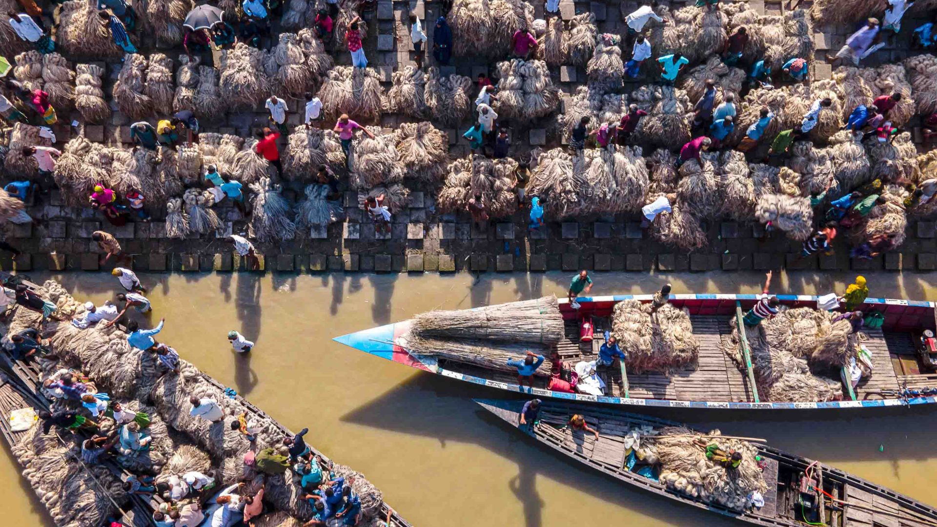 A river market in Thailand shows boats laden with dried grasses.