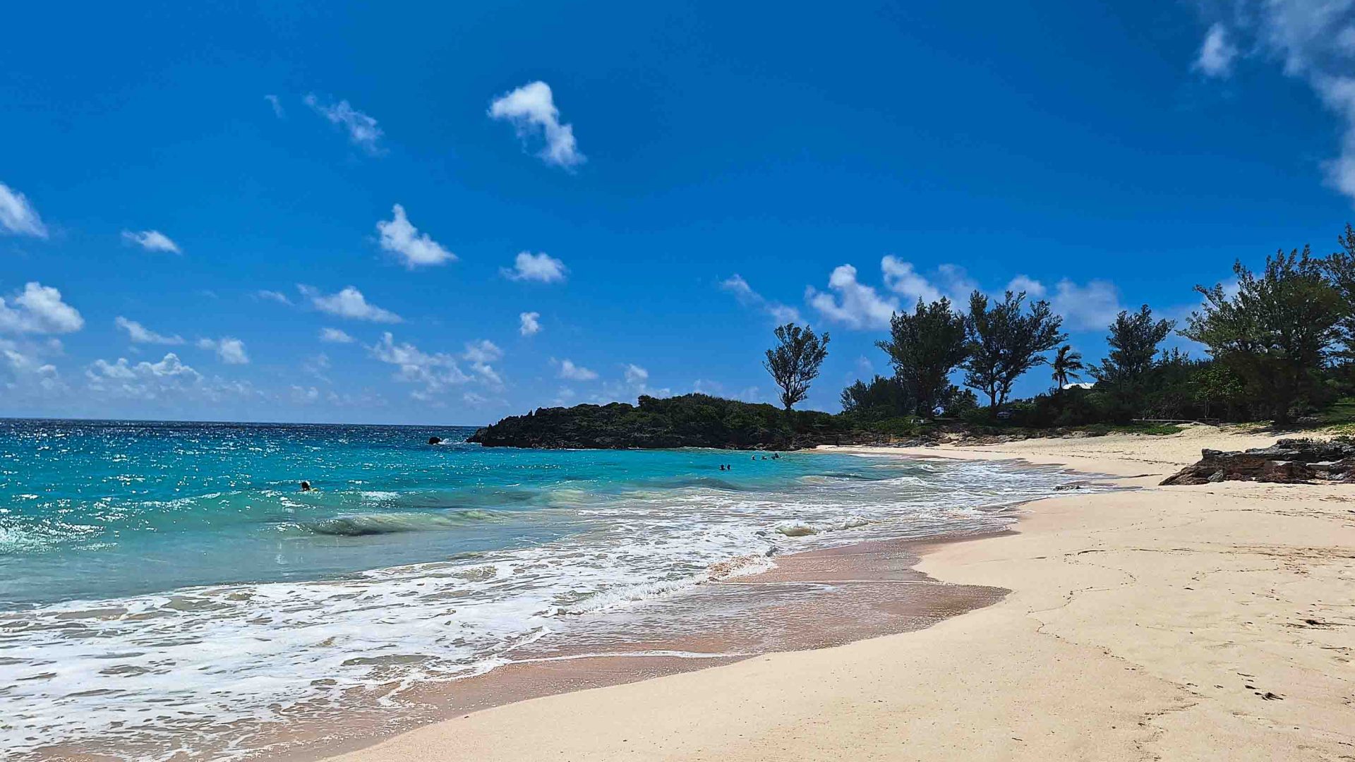 A beach with turquoise water, white sand and a few trees in the background.