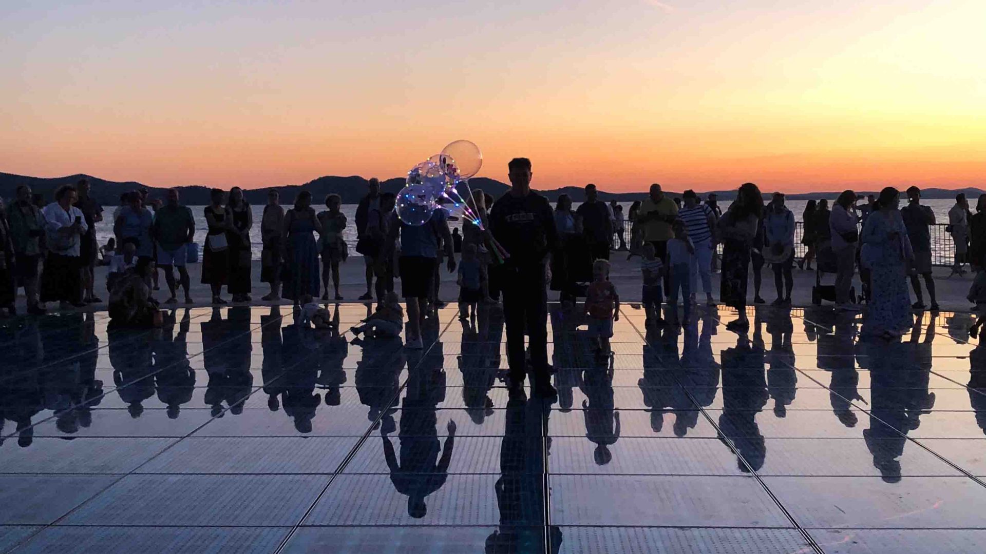 Silhouettes of people and their reflections at sunset.