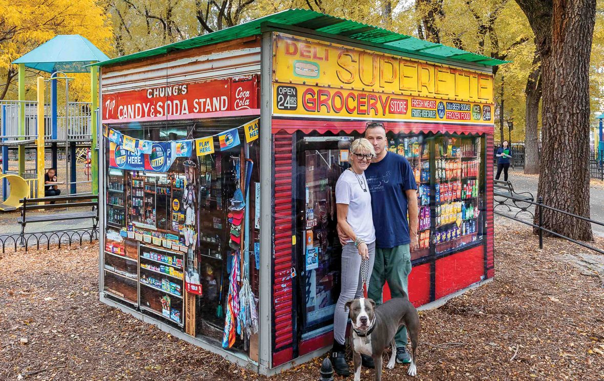 A couple stand outside their brightly painted kiosk.