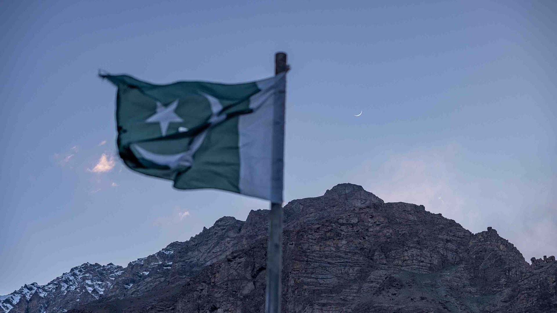 A Pakistani flag is in the foreground and the mountains are in the background.