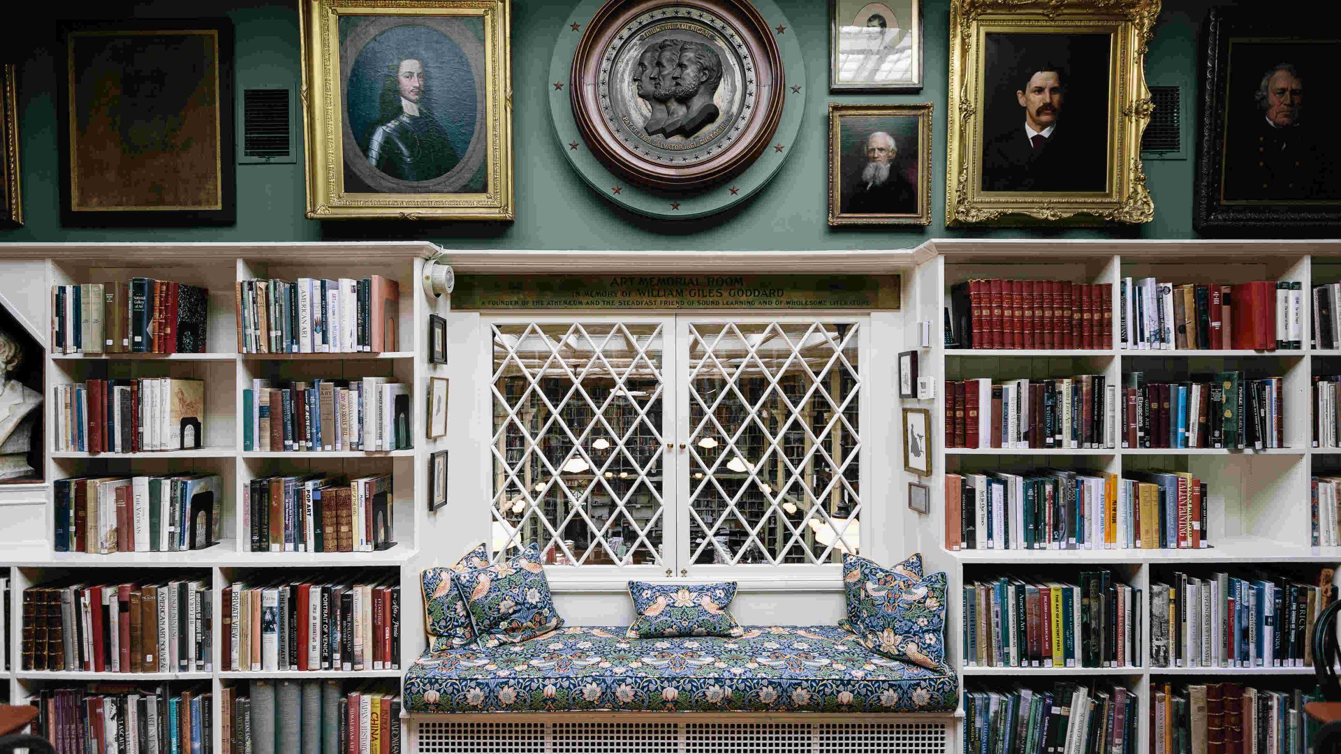 View inside Providence Athenaeum, a historic library. Bookshelves with antique portraits above them