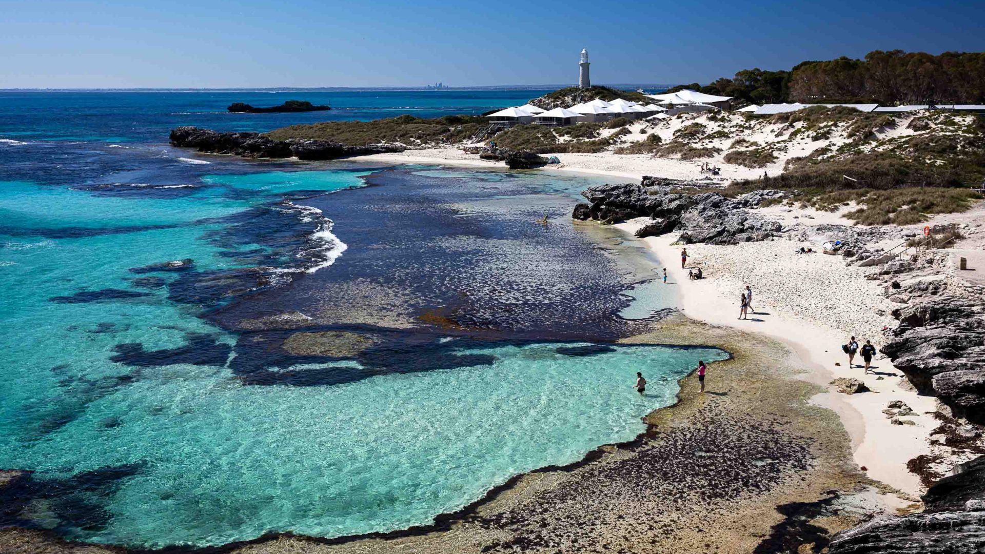 A white sand beach with a few people on it, and turquoise sea.