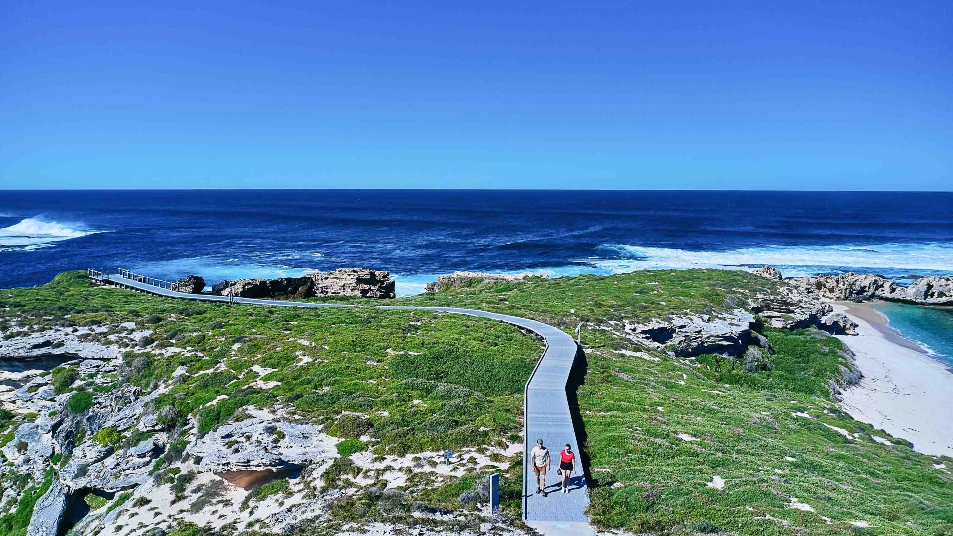 A boardwalk through grass and rocks leads to the sea.