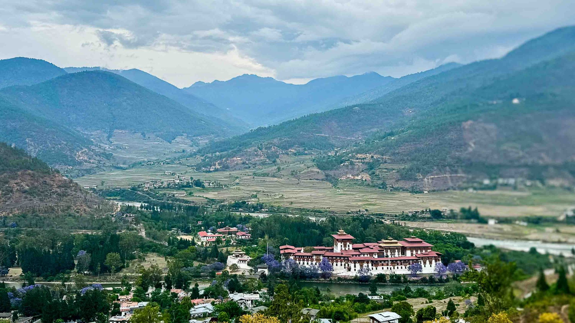 A deep valley with a temple, houses, and mountains in the background.