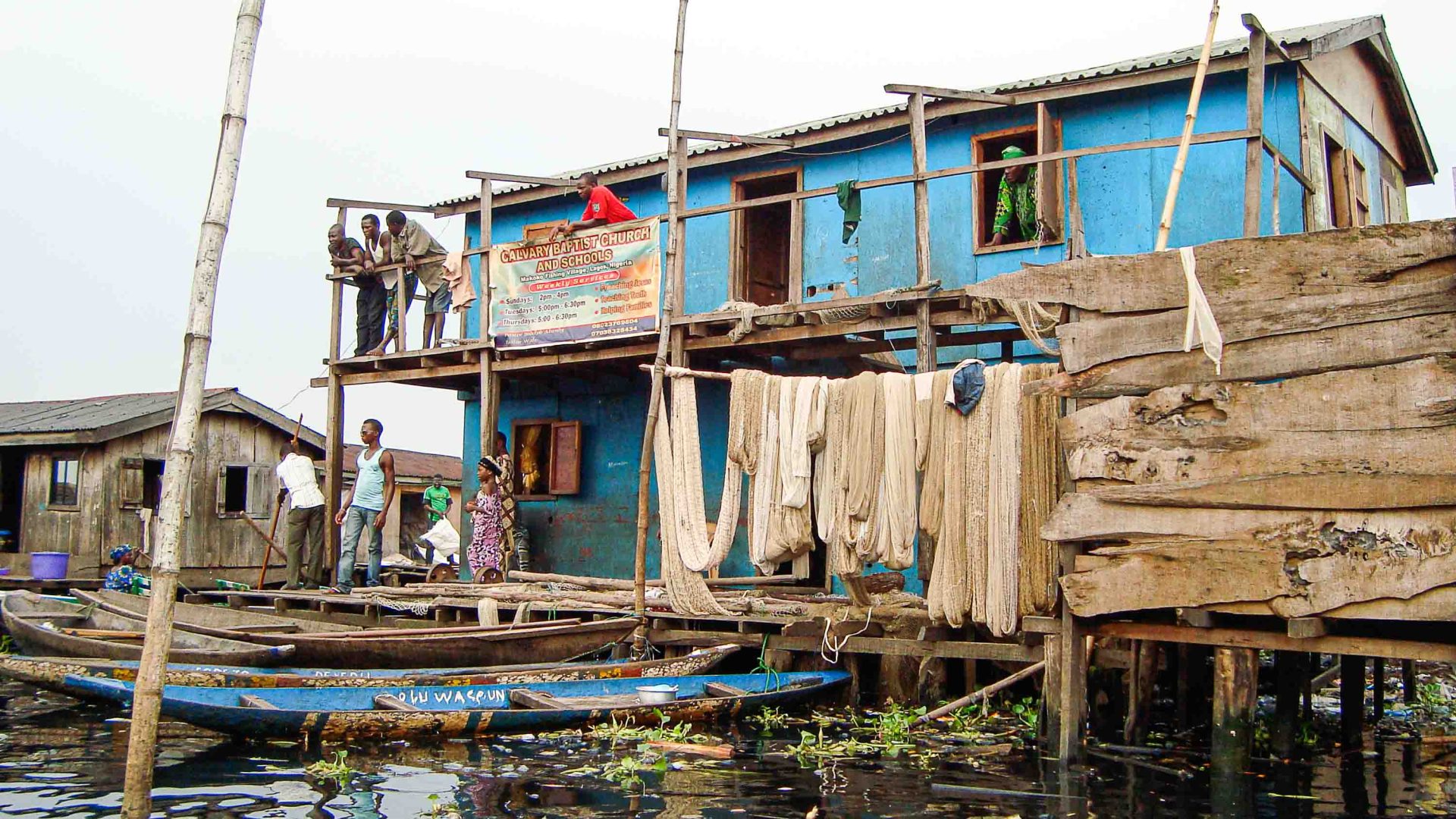 A blue house with people on the desk looking down at a person in a canoe.