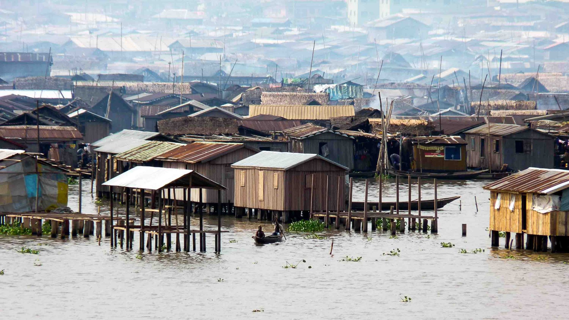 A small boat is rowed past houses in waterways.