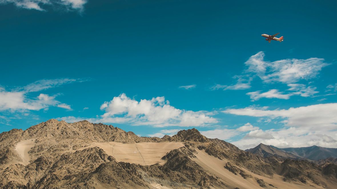 A plane flies over arid mountains.