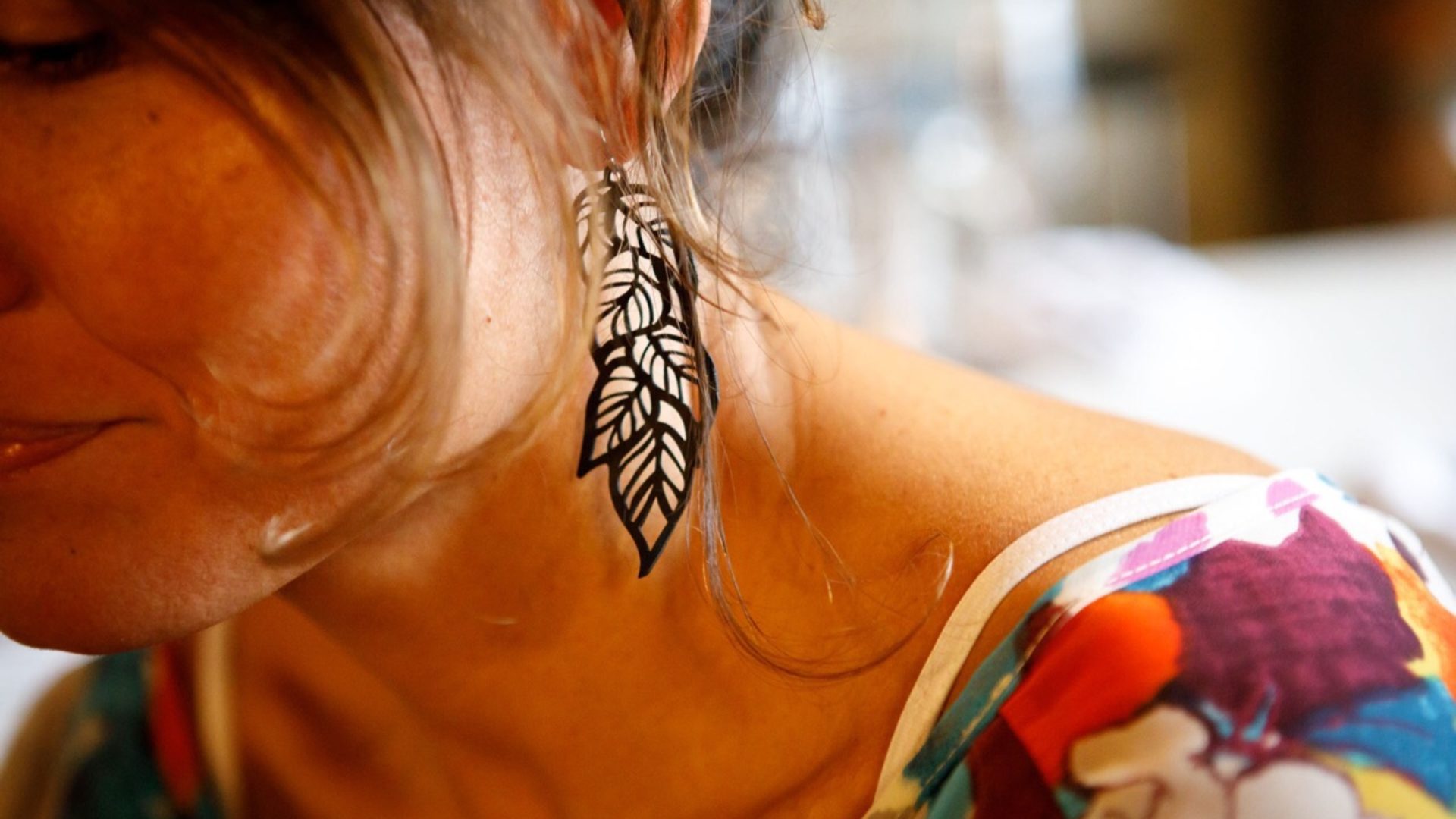 A closeup of dangly black earrings made out of bicycle inner tubes, as worn by someone with their hair tied back.