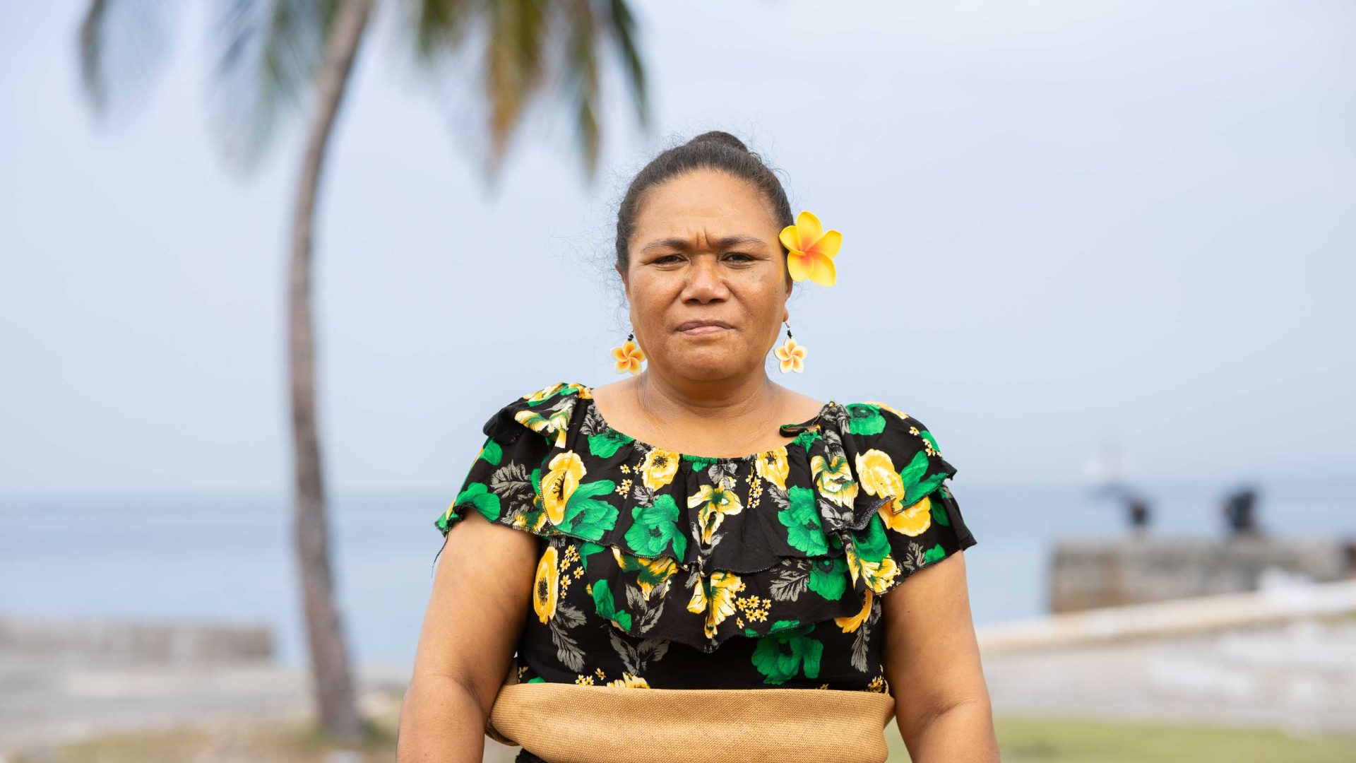 A woman in traditional Tongan attire frowns in a portrait.