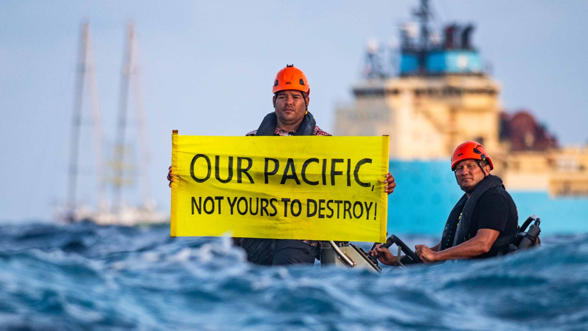 A man in a small boat holds a sign that reads 'Not ours to destroy' with a big ship behind him.