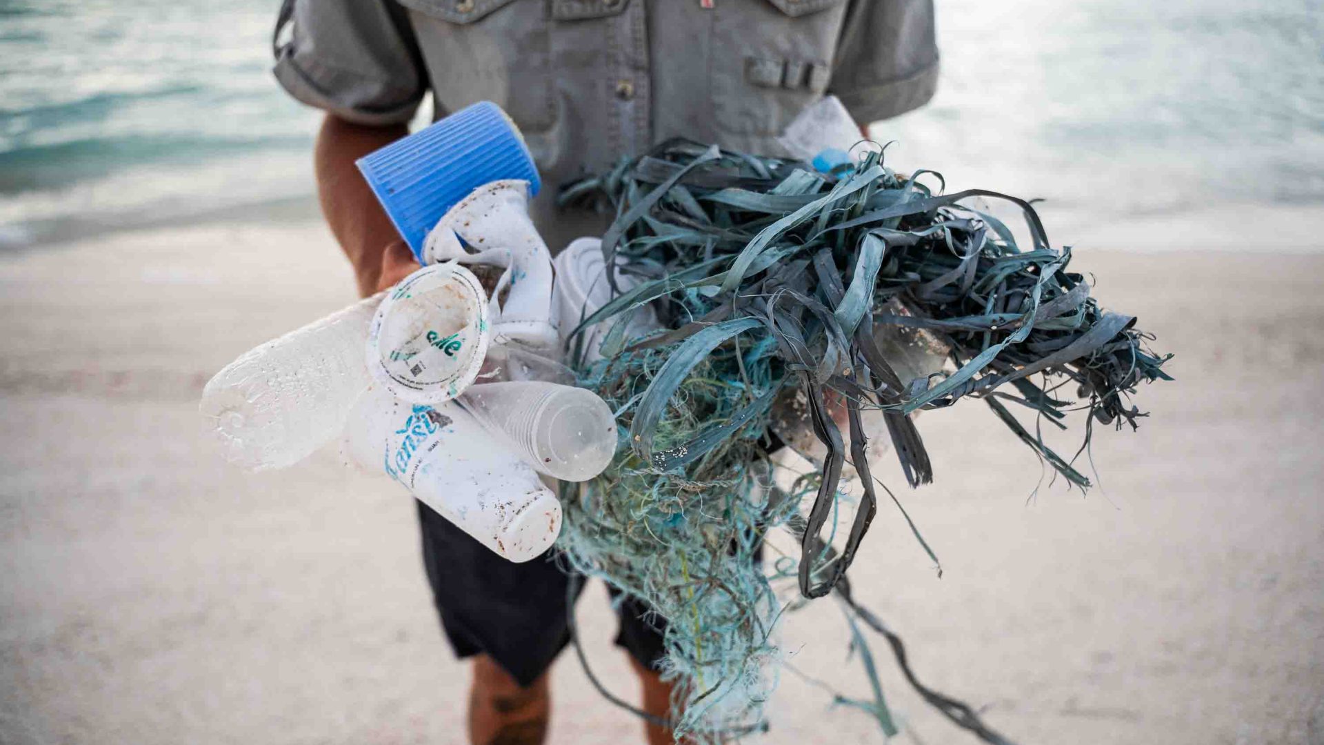 A person standing on a beach holds plastic and waste.