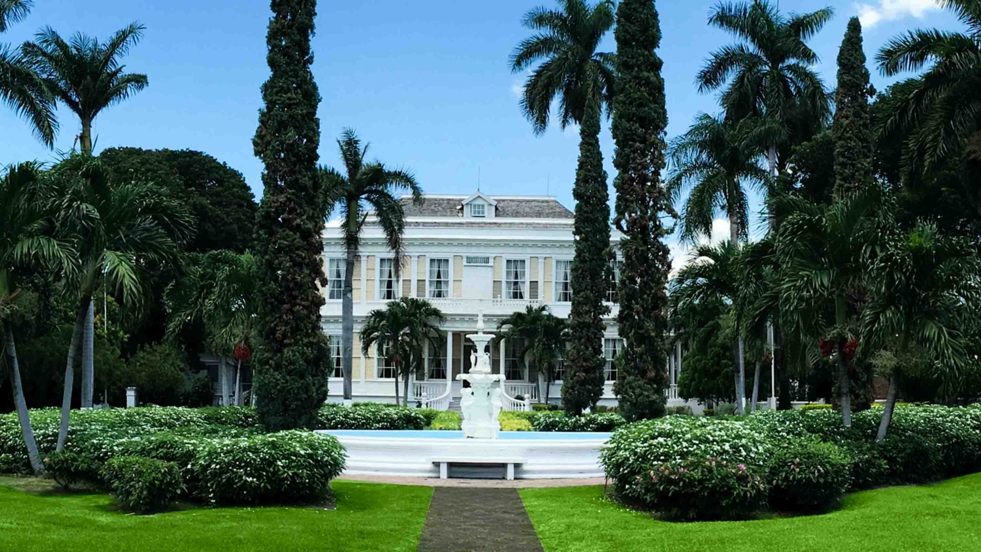 A white mansion in amongst trees and lawns.