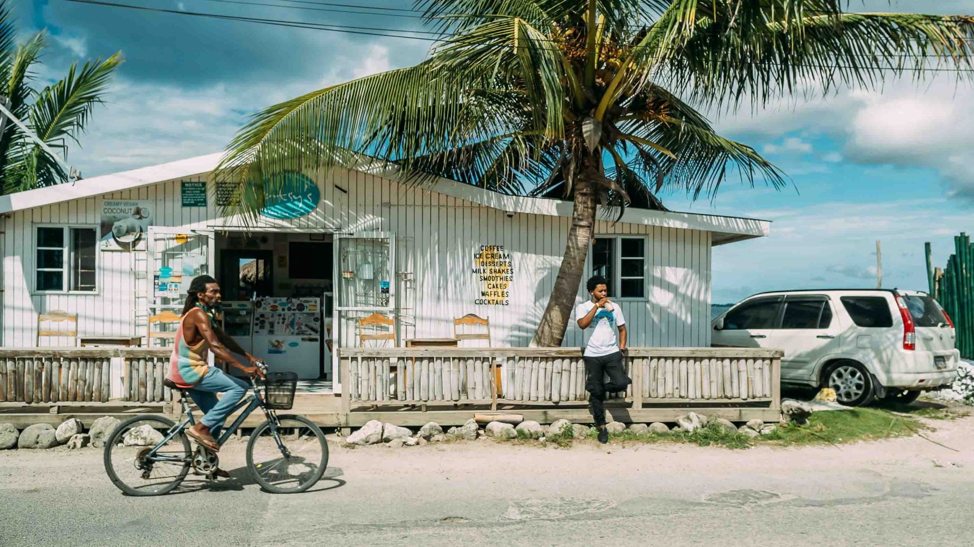 A man rides his bike past an ice cream shop in a coastal town.