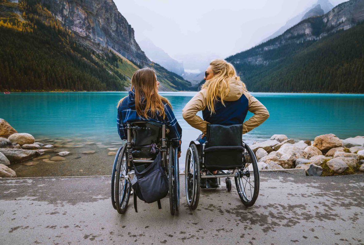 Lisa and Sophie sit in their wheelchairs facing the mountains and Lake Louise with their backs to the camera.