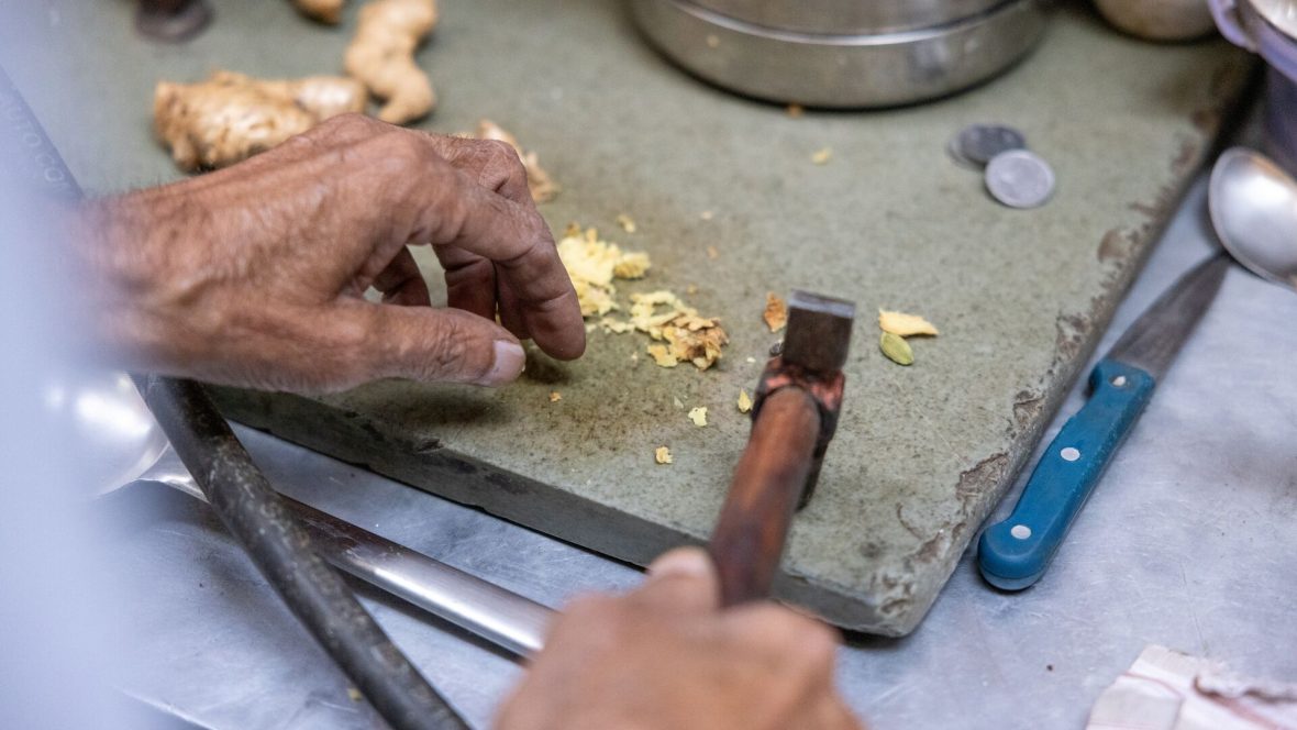 A close-up of a hand chopping ginger on a chopping board