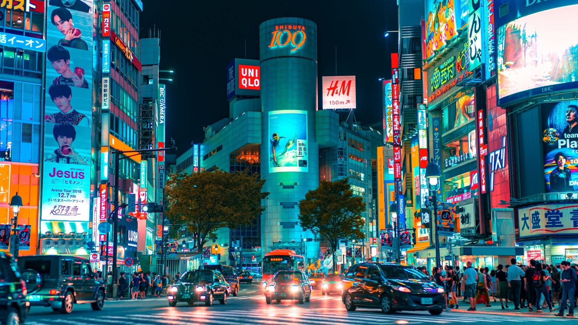 A nighttime view of an intersection in a big city with bright digital billboards.