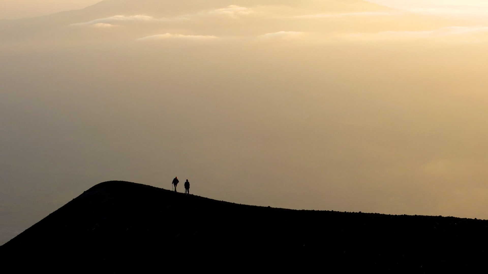 Two figures can be seen walking along the rim of the volcano.