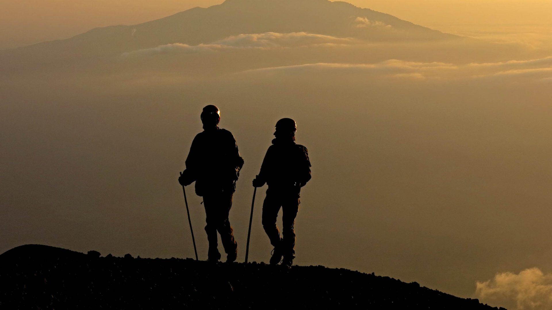 The silhouettes of two people hiking at sunrise.