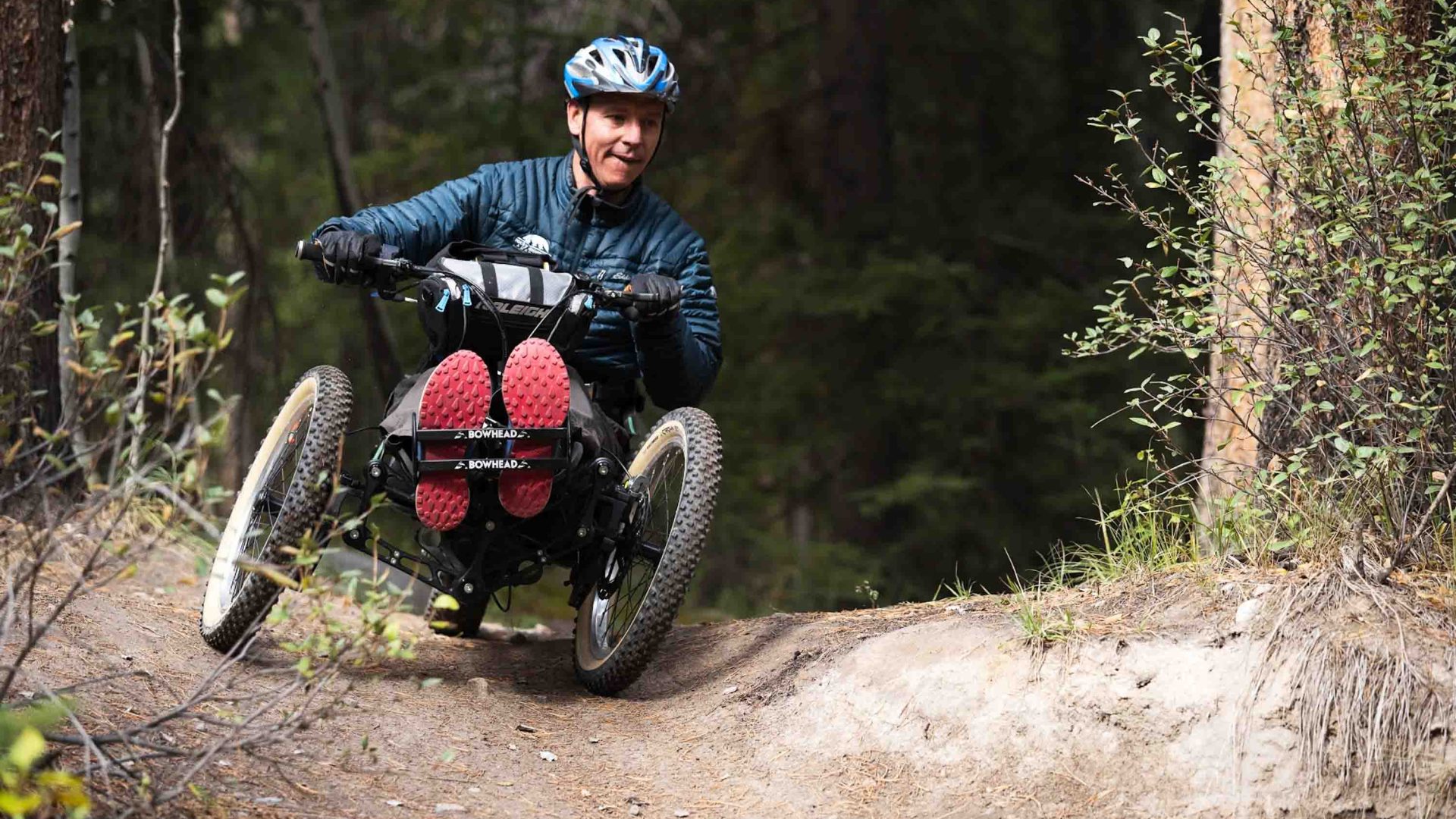 A person in a Bowheads races through trees on a dirt trail.