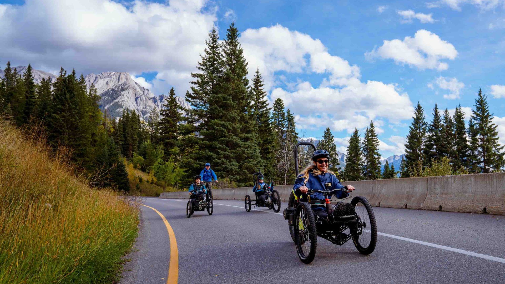 Three people travel down a road in bowhead trikes.