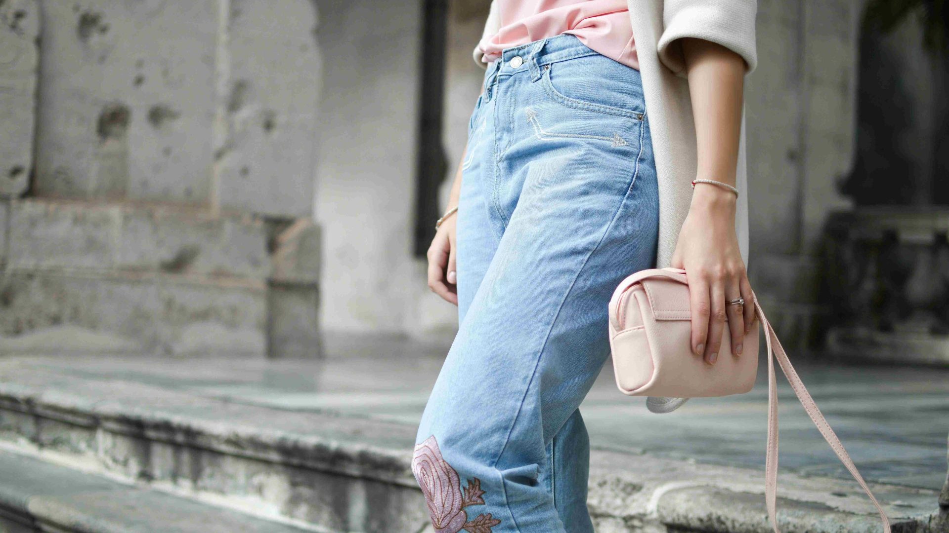 A stylish person from the waist down, wearing a pink shirt and blue jeans.