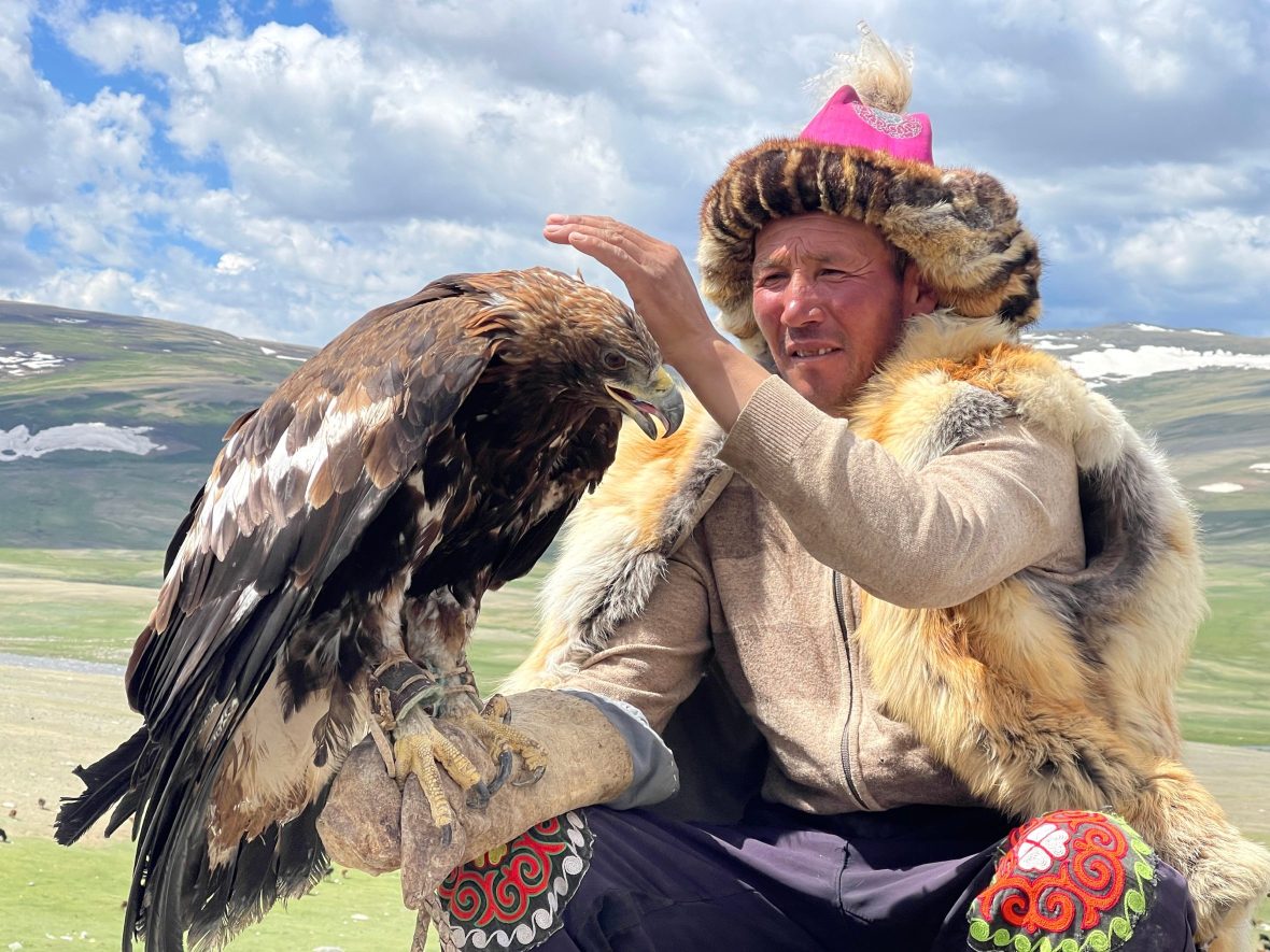 mongolian man wearing traditional dress holds eagle