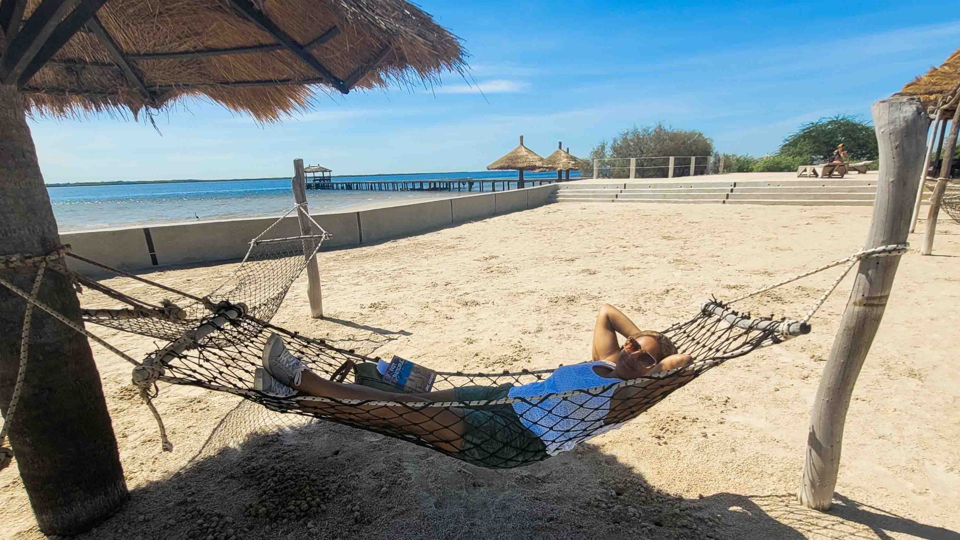 A woman relaxed in a hammock hanging over sand.