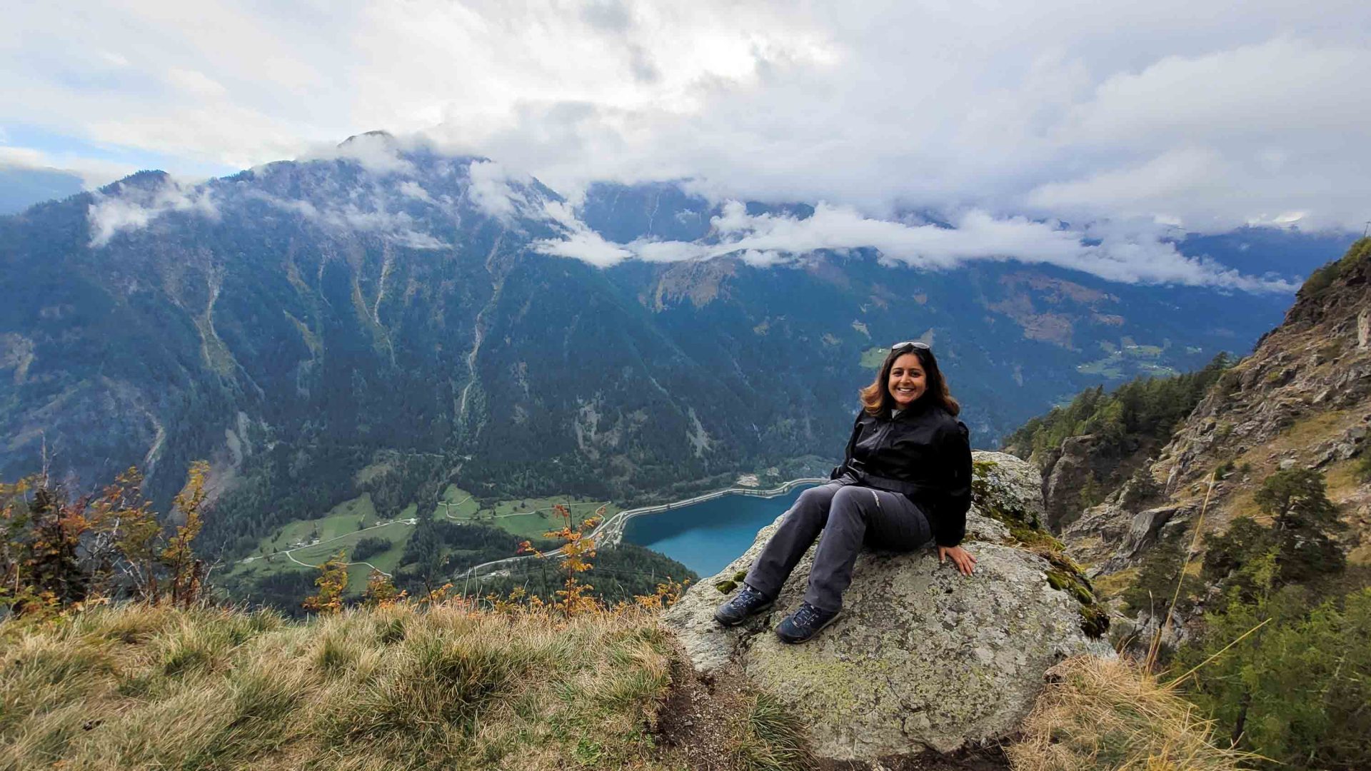 A woman sits on a mountain overlooking a blue lake.