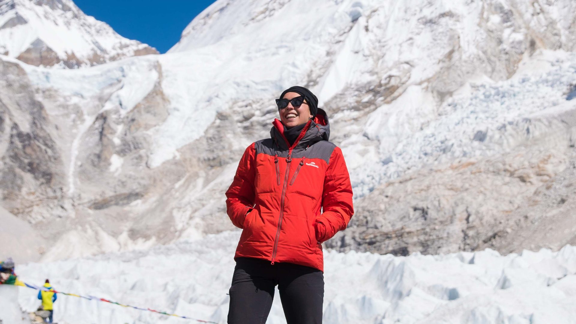 A woman smiles while in front of snow covered mountains.