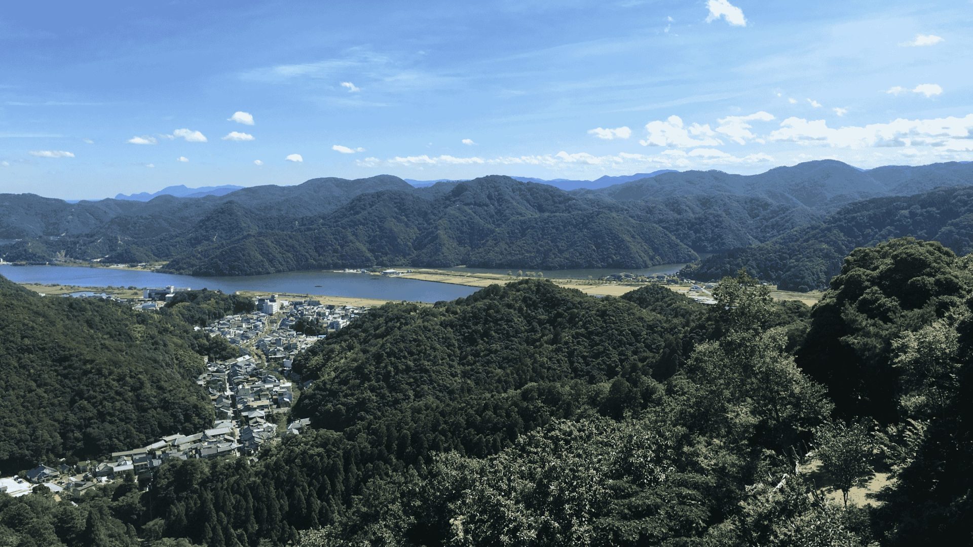 An aerial view of gentle, forested mountains and the seaside in Toyooka, Japan.