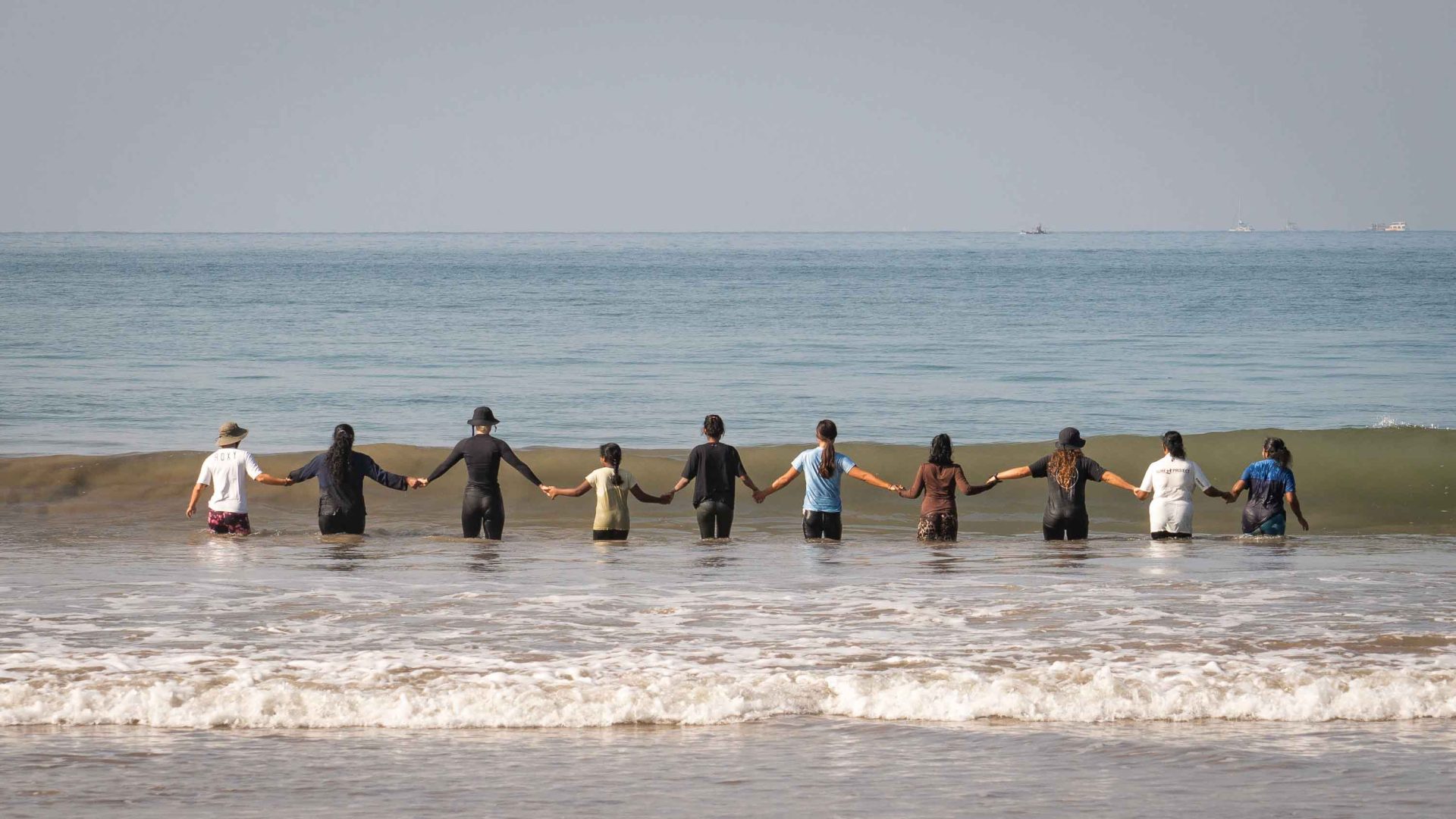 A group of people holding hands walk in to the sea.