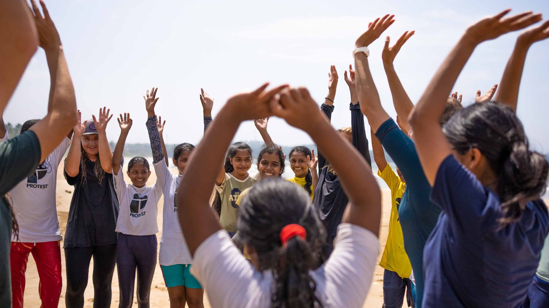 A group of people on the beach all raise their arms in the air.